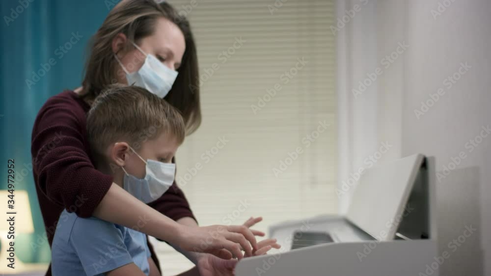 A closeup depiction of a mom in a red coat teaching her blonde little boy how to play the piano while being isolated because of Covid19 infection A closeup depiction of a mom in a red coat teaching her blonde little boy how to play the piano while being isolated because of Covid19 infection