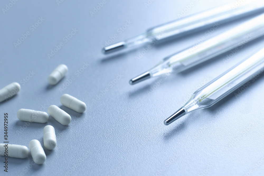 Close-up of a medical mercury thermometer and white capsules