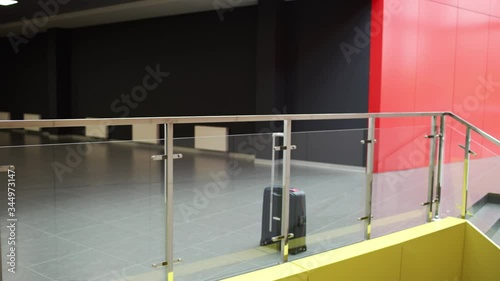 Bearded brunette man is looking at his watch and going away leaving his suitcase near glass fence in modern building. Young guy forgot his bag in contemporary business center or mall.