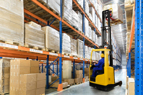 Huge distribution warehouse with high shelves and forklift with driver.