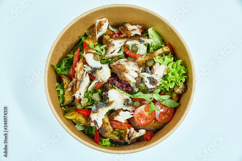 Sea fish salad with cherry tomatoes, capers, grilled vegetables, lettuce in a cardboard box