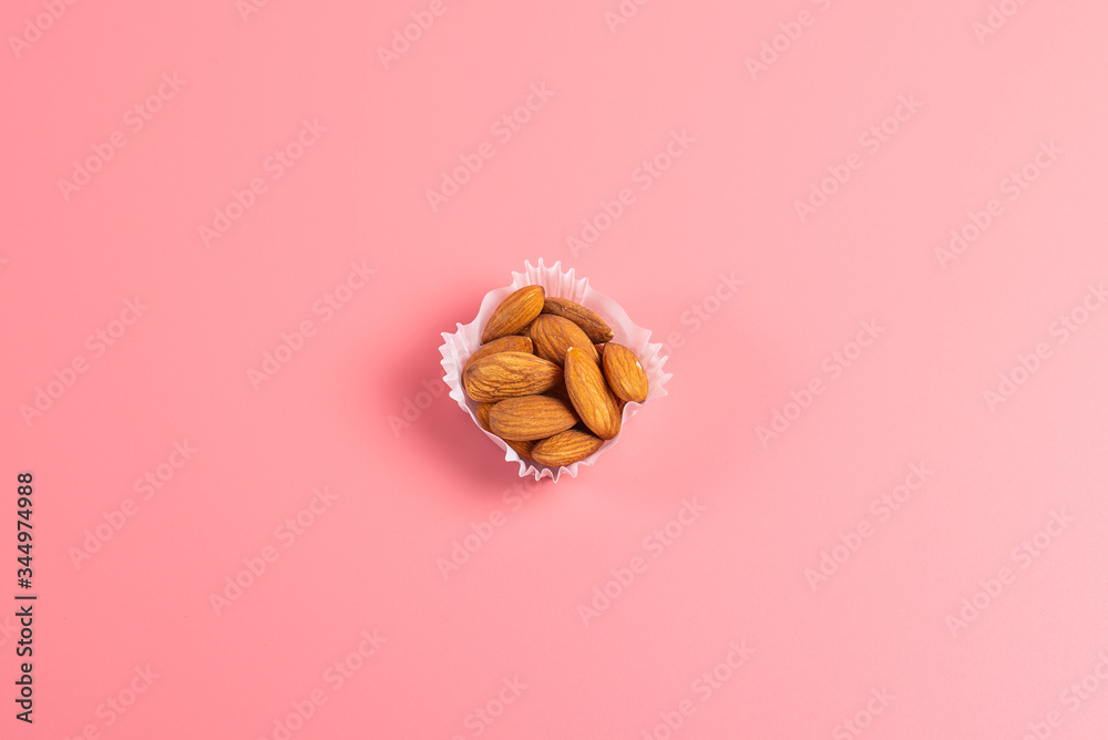 a portion of almonds in a paper cupcake mold on a pink background a portion of almonds in a paper cupcake mold on a pink background