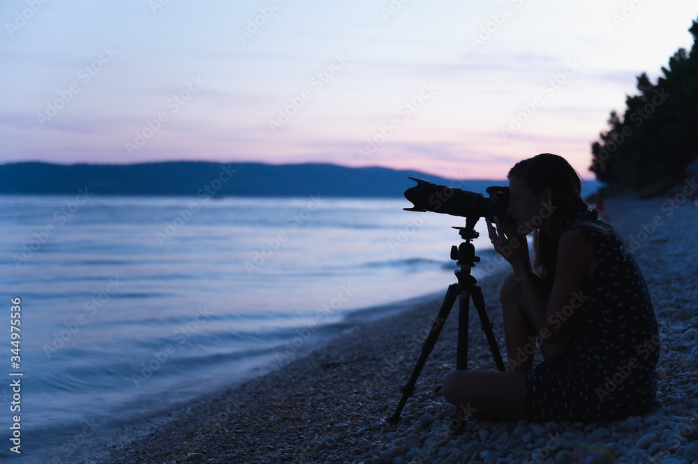 Young female photographer sitting on the beach with camera on tripod
