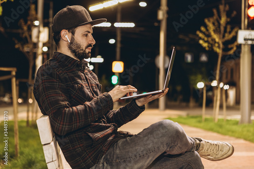 attractive young businessman working on startup sitting with laptop on the street. Freelance work concept.