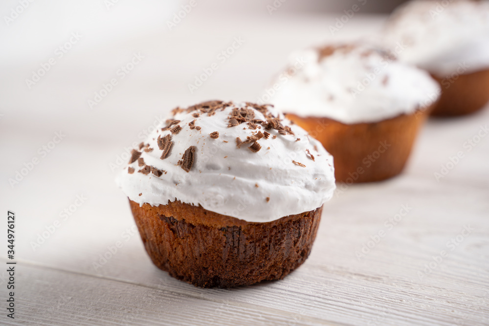 Cupcakes with whipped cream and chocolate chips on a white wooden table. Image for the menu or catalog of confectionery products. Cupcakes with whipped cream and chocolate chips on a white wooden table. Image for the menu or catalog of confectionery products.