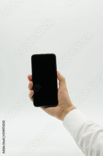 The man holds a black phone with black screen on white background in front of him