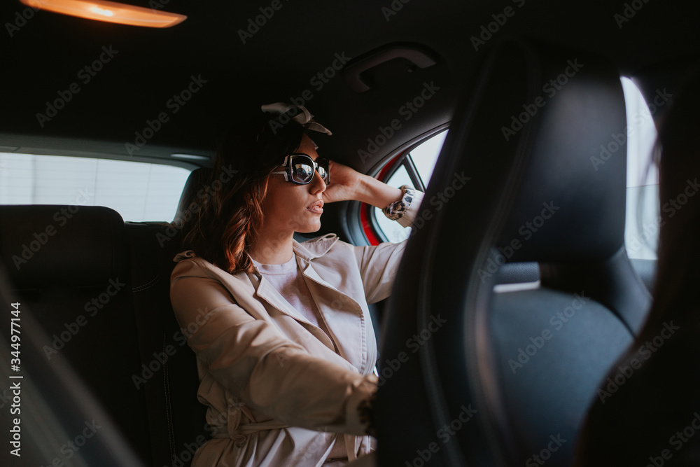 Beautiful caucasian businesswoman with sunglasses sits in the back seat in a red car