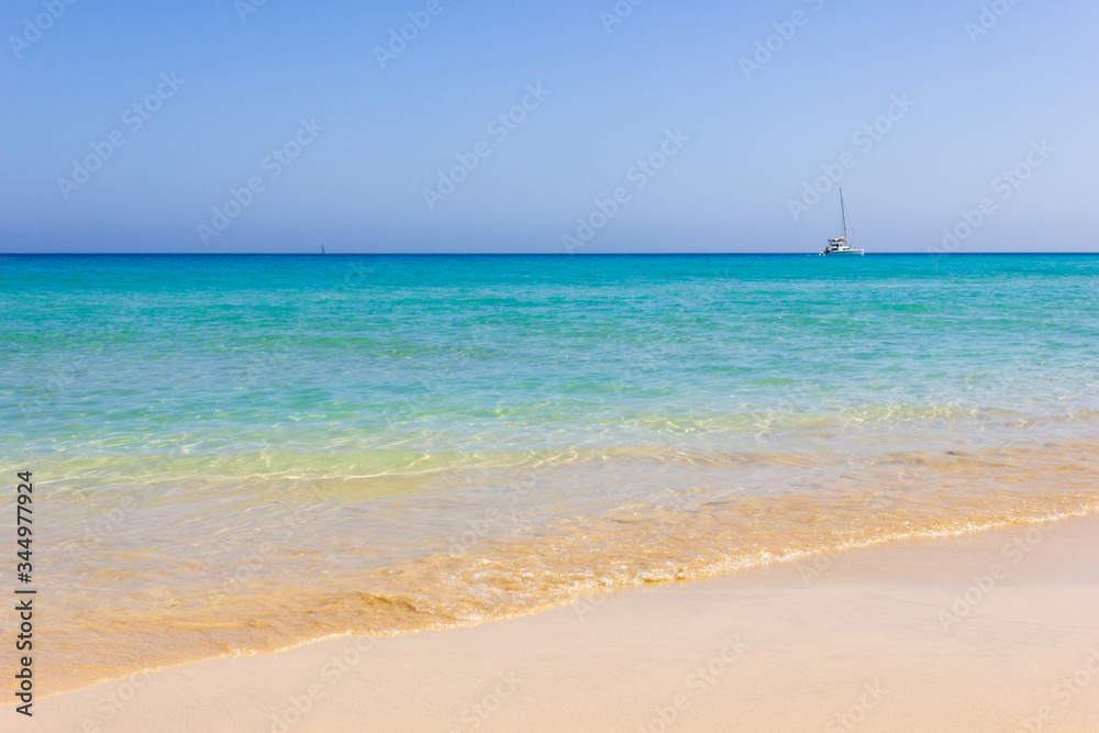Sailing boat far away on turquoise water empty beach in Fuerteventura. Idyllic natural landscape view from seashore. Summer travel, secluded in paradise concepts