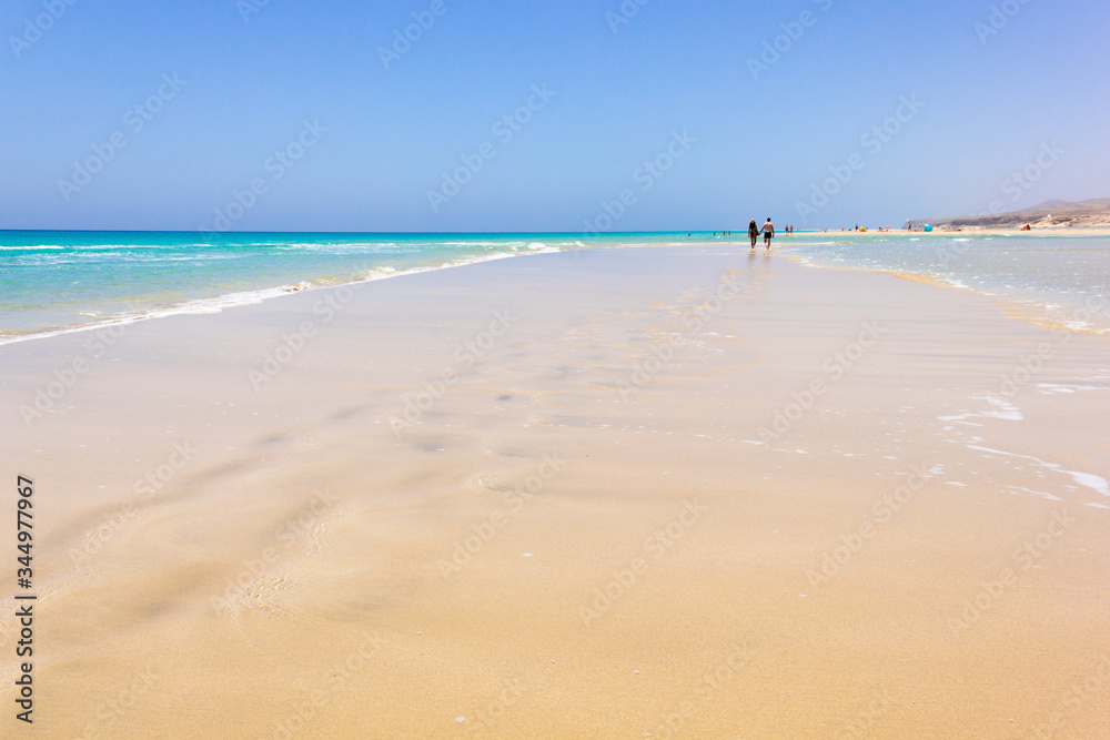 Calm seashore at Sotavento beach on sunny day in Fuerteventura, Spain. Couple on distance at Jandia coastline in Canary Islands. Paradise destination, summer vacation, natural landscape concepts