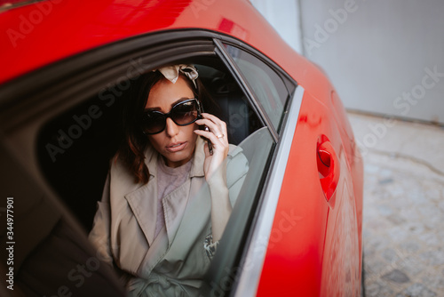 A beautiful caucasian businesswoman with a phone in her hand sits in a red car © Dragica