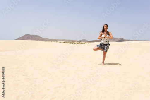 Smiling yogi doing vrksasana on empty desert in Corralejo Natural Park. Middle aged woman practicing tree yoga balance pose on sand dunes in Fuerteventura island, Spain. Hope, metaphor concepts