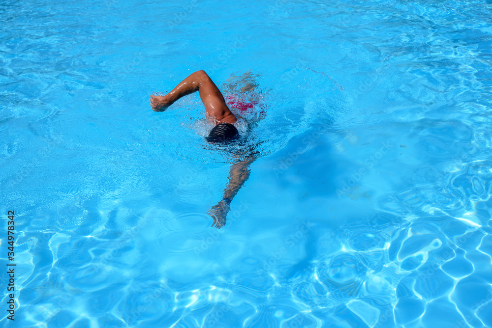 Caucasian man swims in freestyle (crawl) at the outdoor swimming pool on a sunny summer day