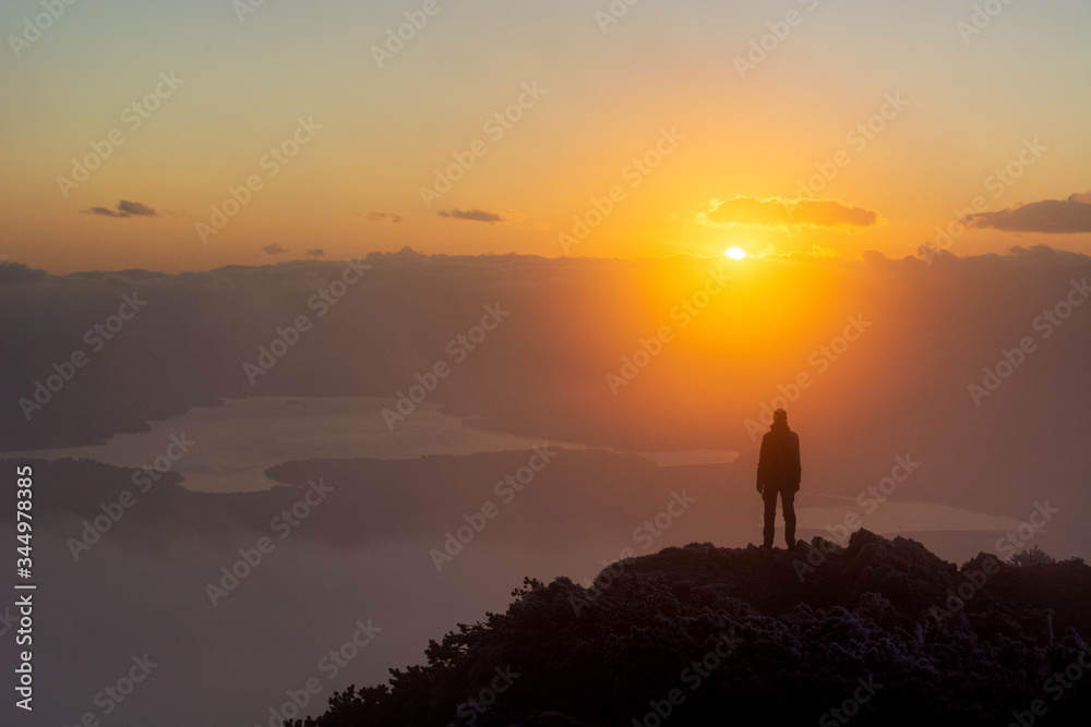 silhouette of a man standing on a mountain top with sunrise in background