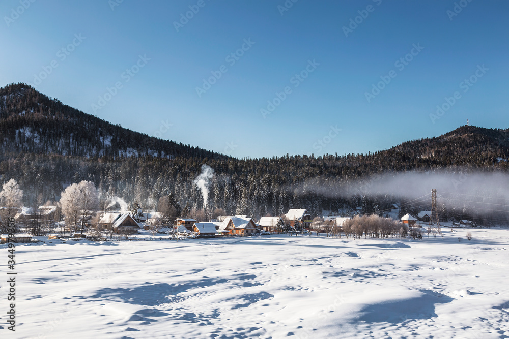 Winter landscape with the village of iogach on the background of forested mountains. Altai Republic, Russia