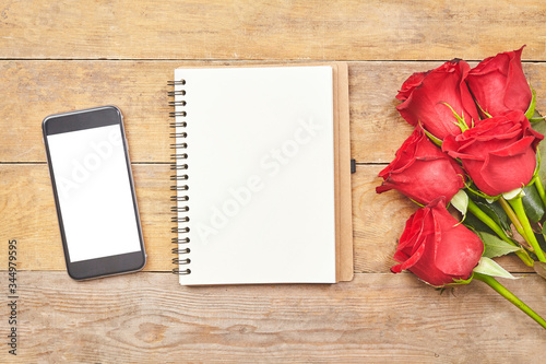 Surface of a wooden table with smartphone, red rose and notebook paper