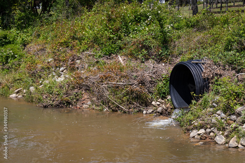 фотографія Water entering a stream from a black drainage pipe, runoff environmental polluti