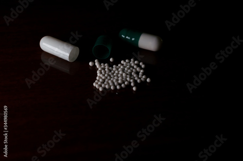 open white and green medicine capsule, showing the small particles that exist inside each capsule, opened pill, Concept photo with dramatic light, copy space and black background