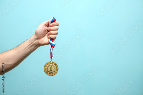 the male hand of the winning athlete holds the gold medal on a blue background space for text