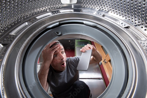 Worried caucasian man taking out a phone from the drum of the washing machine. Interior view. photo