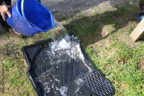 a man washes car mats. pours water from a blue bucket on the salon floor mats. it washes the dirt off them.
