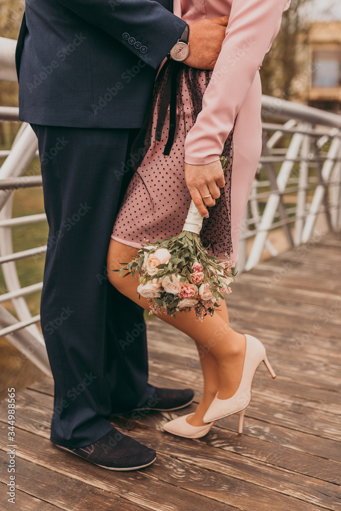 Close up male and female legs, newlywed standing on a wooden bridge and bride holding a bouquet. Wedding day
