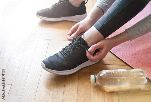 Close up shot view of fit woman tie shoelaces while doing workout at home. Bottle of water. Athletic female tying the laces on shoes while taking break between training at home
