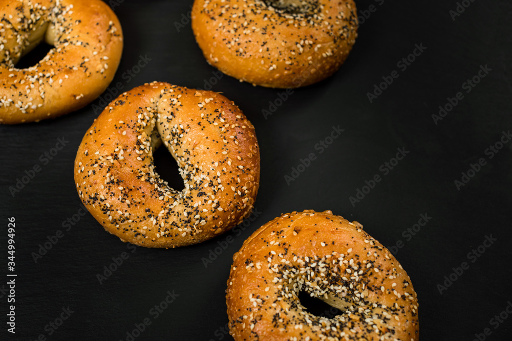 Freshly Baked Bagels Topped with Sesame Seeds, Poppyseeds, Garlic and Onion on Black Background. Selective focus. Freshly Baked Bagels Topped with Sesame Seeds, Poppyseeds, Garlic and Onion on Black Background. Selective focus.