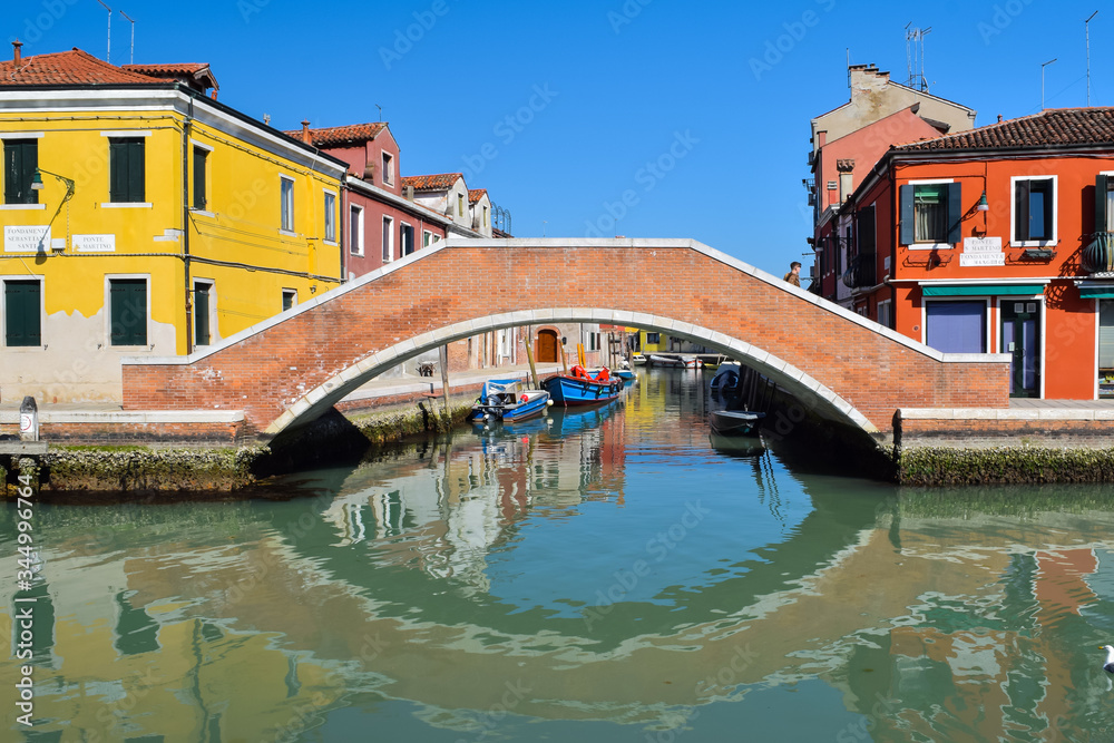 Picturesque Venetian canals with bright colorful buidlings and bridge on the blue sky background