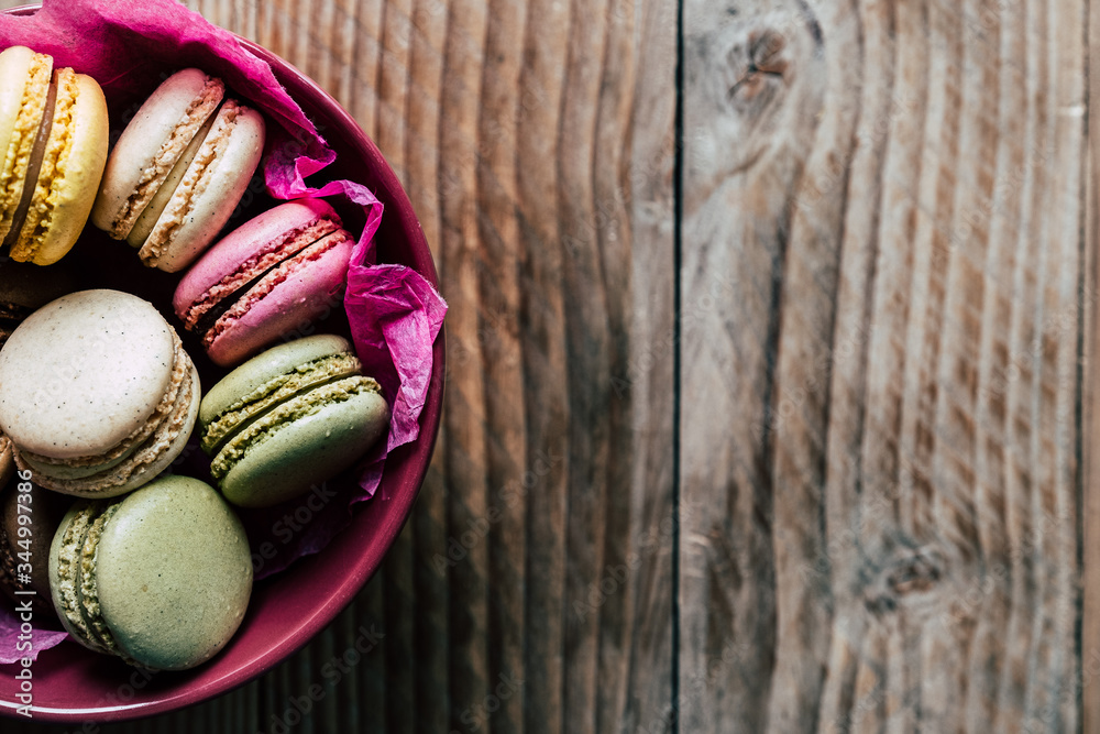 Macarons colorés dans un bol rose sur un fond en bois