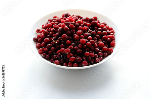 A lot of frozen cranberries in the white dish on a white table