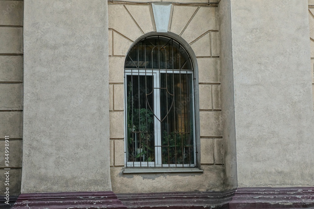 one white window behind the iron bars on the brown old concrete wall of the building one white window behind the iron bars on the brown old concrete wall of the building