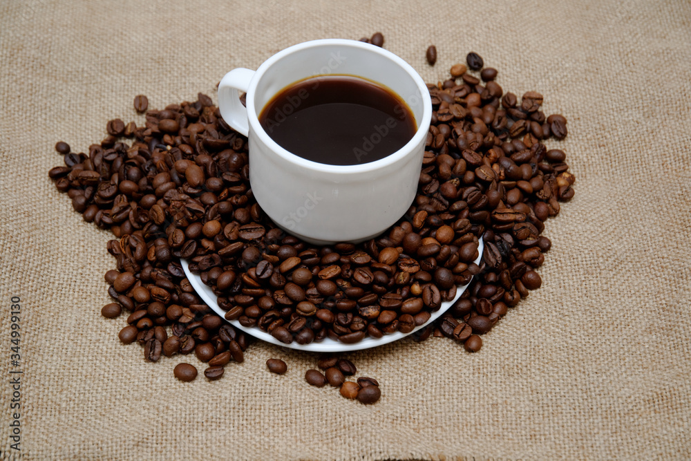 coffee beans sprinkled on a white saucer from above a cup with coffee. coffee beans sprinkled on a white saucer from above a cup with coffee.