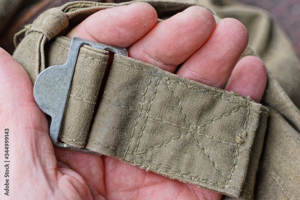 Obraz premium fingers hold a gray iron carbine on an old green harness made of fabric on a backpack