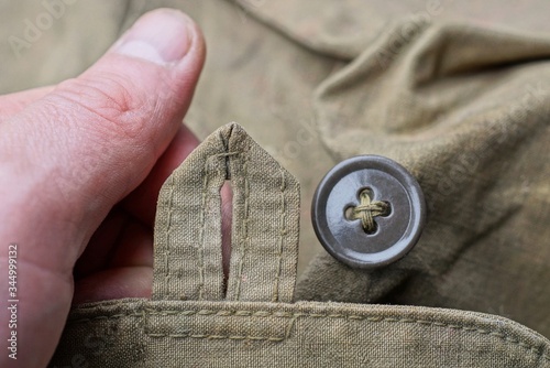 fingers hold a green fabric buttonhole and a brown plastic button on old clothes photo