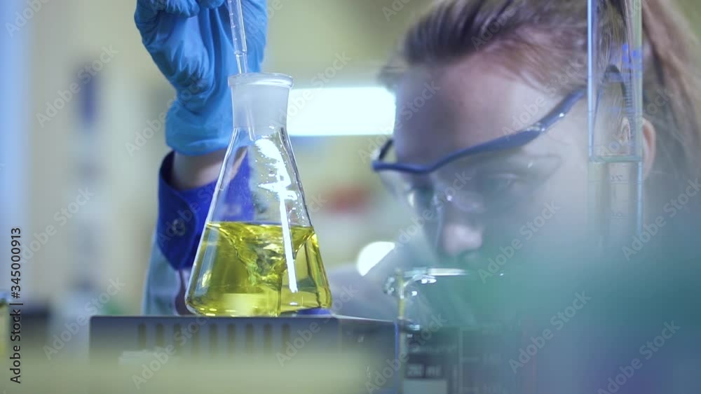 female chemist pour liquid in flask with pipette. Spbd Yellow liquid is mixed in a glass beaker in a laboratory. color change in laboratory. concept research, analysis, experiment. reaction on stirrer