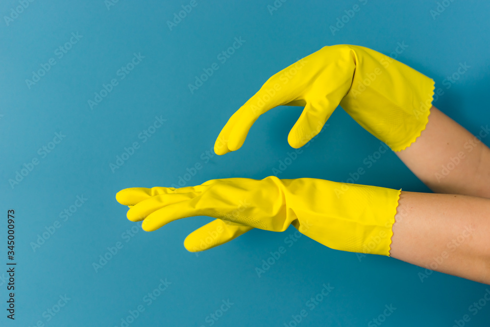 Fototapeta Close up on hand of unknown caucasian woman female girl putting on protective yellow rubber gloves to clean or disinfection against blue wall background in day looking tired side view