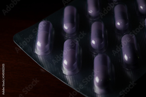 purple vitamin or medicine, food suplements,  capsule (pills) inside the transparent plastic pot, concept of health and body care, with dramatic light, copy space and black background