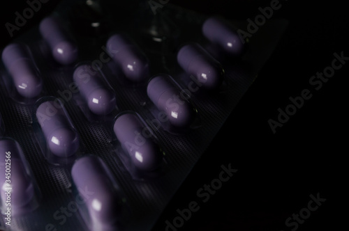 purple vitamin or medicine, food suplements,  capsule (pills) inside the transparent plastic pot, concept of health and body care, with dramatic light, copy space and black background