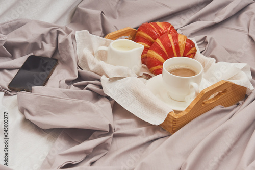 Breakfast on a crumpled bed, coffee, croissants, mobile phone