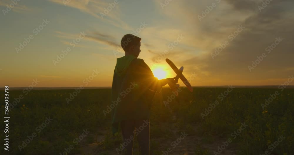 A boy is standing on the field and playing with a plane. Sunset. 4K A boy is standing on the field and playing with a plane. Sunset. 4K