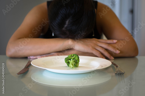 Fotografie Depressed woman hungry from dieting, sitting in front of a empty plate