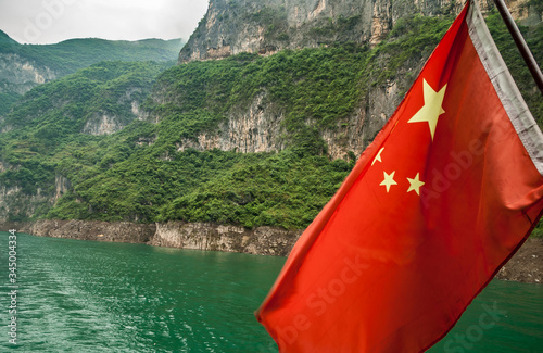 Wuchan, China - May 7, 2010: Dawu or Misty Gorge on Daning River. Red Chinese flag over emerald green water and green foliage covered flanks of mountains as backdrop. photo