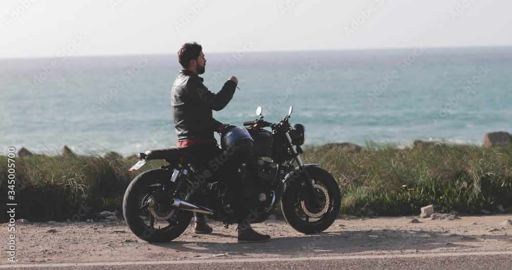 Man removing helmet on classic motorcycle by the seafront Man removing helmet on classic motorcycle by the seafront