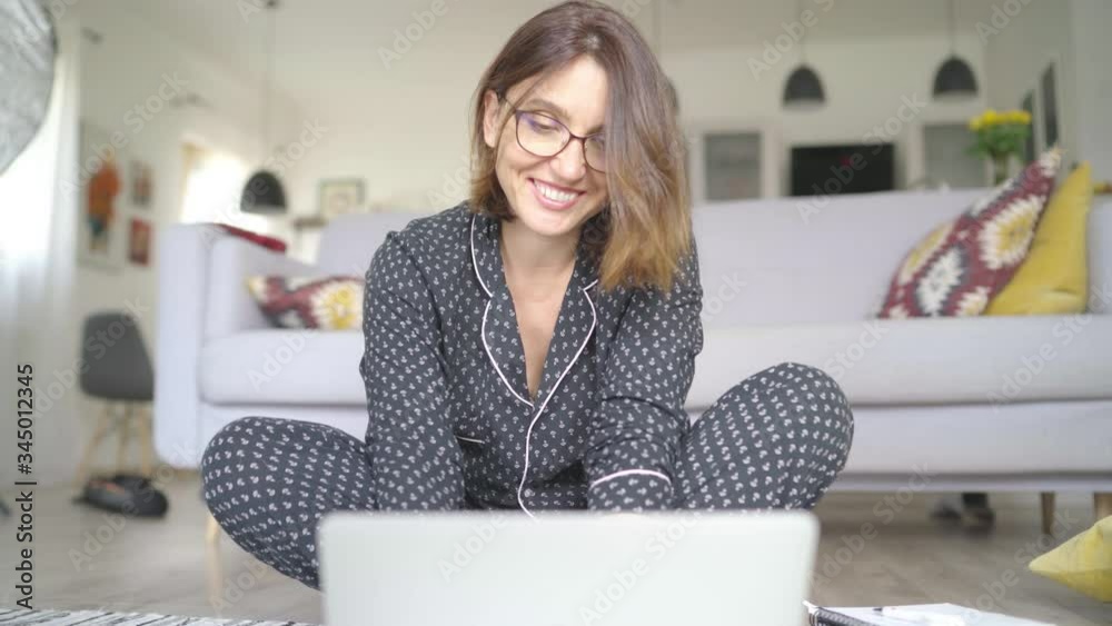 4K young brunette woman sitting on floor at home in her pajamas browsing on laptop. Lockdown, isolation concept. Home office concept.