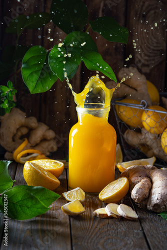 Fresh tropical juice of lemons and ginger surrounded by leaves, lemon slices and ginger roots. Summer detox and vitamin C concept. Vertical format, cook book concept photo