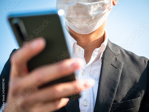 スマートフォンを操作するマスクをしたビジネスマン
