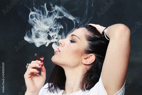 Beautiful european bossy brunette girl smoking a cigarillo like a boss in studio on isolated background. Modeling, style, fashion concept. Noir moments, retro style photography.