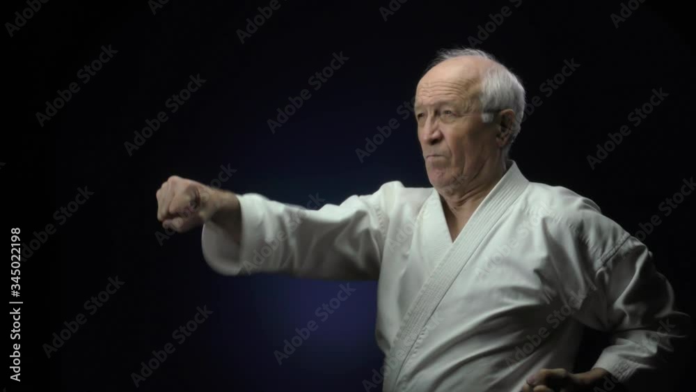 Old man athlete makes blocks and punches against a dark background Old man athlete makes blocks and punches against a dark background