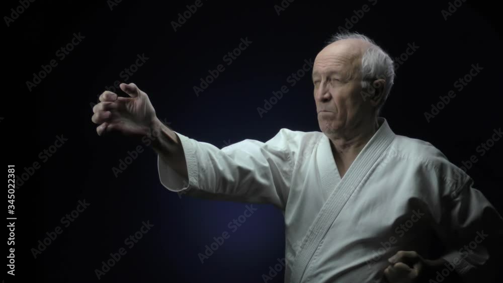 Old man athlete trains punches against a dark background Old man athlete trains punches against a dark background