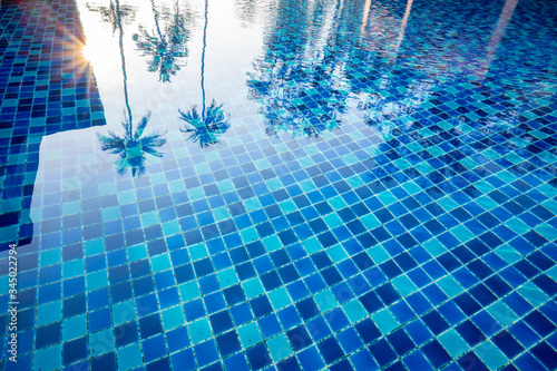 Obraz na płótnie The clear water in the blue pool in the morning is reflected by the coconut trees and the yellow sunlight, the concept of relaxing days and happy holidays in bright colors. w salonie